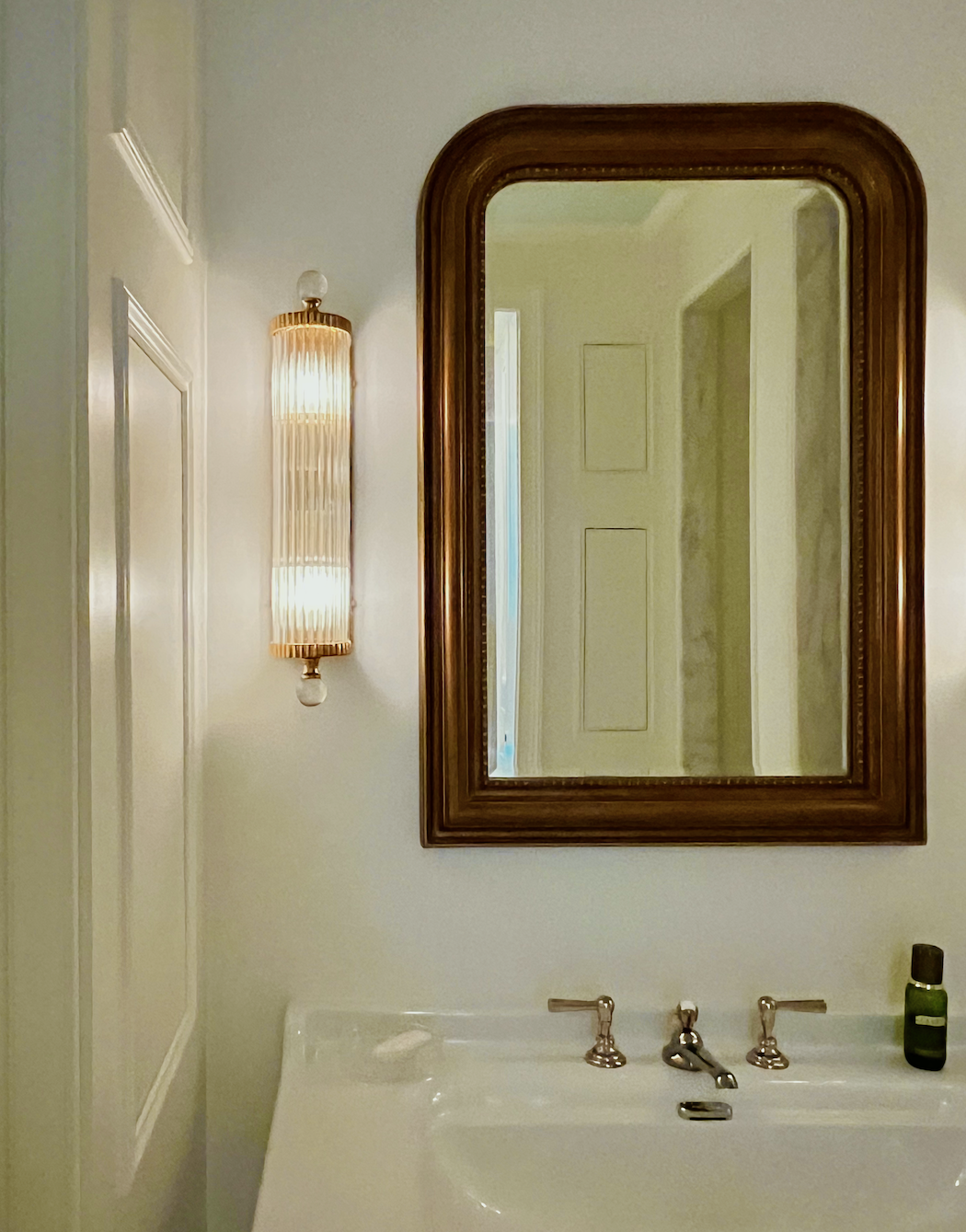 Close-up Vignette primary bathroom mirror + sconce + sink + faucet